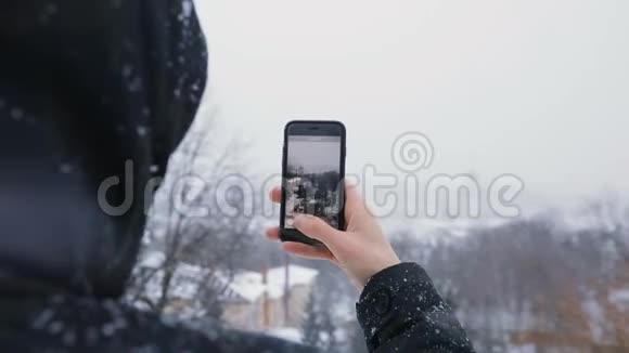 穿着黑色引擎盖的人使用电话显示了老城区和白雪皑皑的冬季公园的美景慢动作视频的预览图