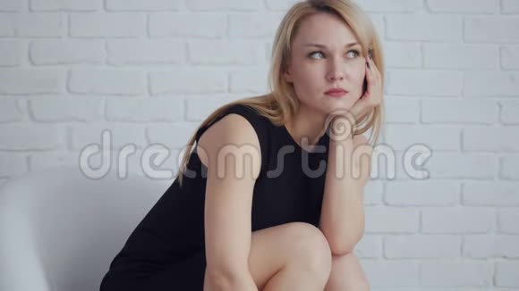 年轻的金发碧眼的女人穿着黑色连衣裙独自坐在房间里视频的预览图