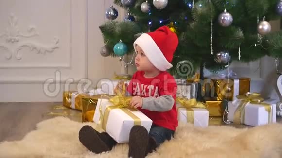 穿着圣诞帽和蝴蝶结的可爱男孩在礼物上系丝带视频的预览图