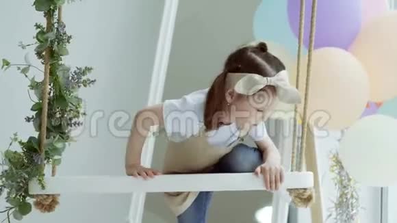 一个小女孩爬上秋千小女孩在工作室里荡秋千摇摆的孩子视频的预览图