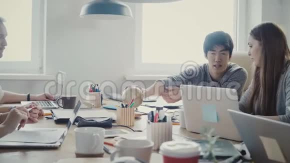 快乐的亚洲商人带着一个小小的地球仪在多民族的办公会议上在4K的阁楼办公视频的预览图
