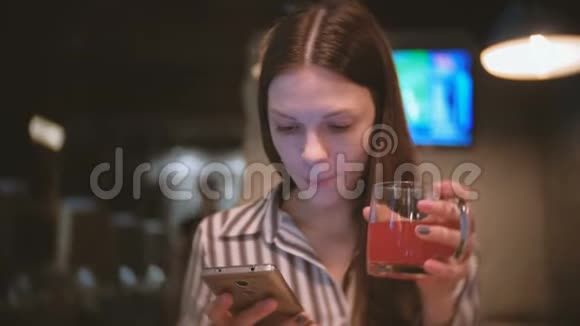 年轻漂亮的黑发女人在手机里读东西在咖啡馆里喝红凉茶视频的预览图