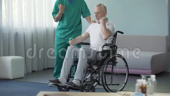 在护士的帮助下坐轮椅的男性在按摩他虚弱的肌肉视频的预览图