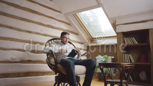 戴眼镜的成年男子在阁楼上看书和喝咖啡视频的预览图