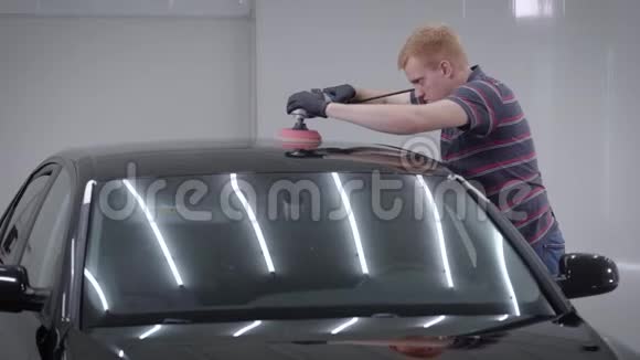 站在车库的成年男子侧视汽车车顶使用抛光机视频的预览图