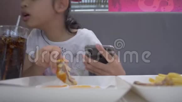 亚洲可爱的女孩一边吃食物一边用手机视频的预览图