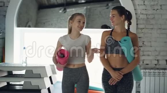 多莉拍了一张年轻女人的照片她们一起在健身房散步有感情地交谈女人手里拿着瑜伽垫视频的预览图