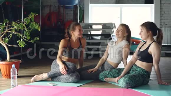 快乐的女孩在健康中心社交坐在木地板上的瑜伽垫上体育器材绿色植物视频的预览图