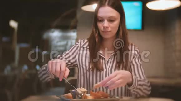 年轻漂亮的女人深色头发用刀子在咖啡馆里的一块面包上抹上小胡子她吃三明治视频的预览图