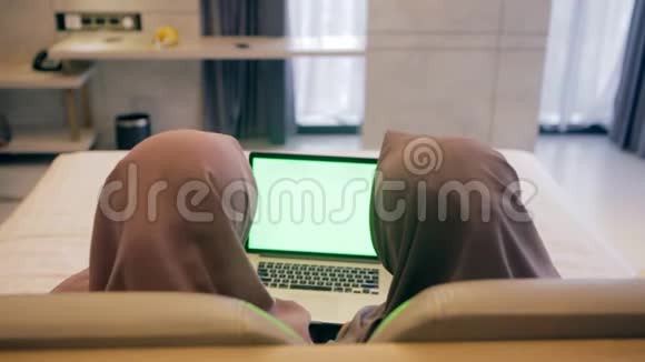 两位年轻的穆斯林妇女用绿色屏幕在笔记本电脑上观看视频的后视图视频的预览图