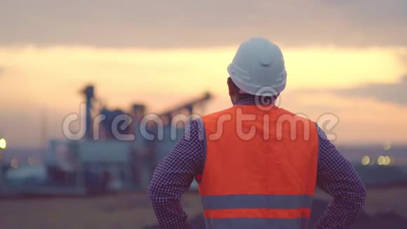 日出时炼油厂的天空背景轮廓和发电厂模糊波克戴着头盔的工程师视频的预览图
