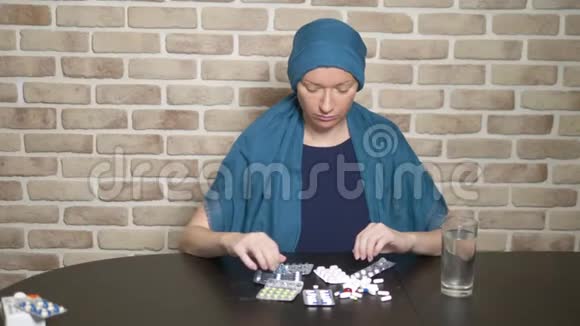 一个戴头巾的女人一个癌症病人接触药丸坐在靠砖墙的桌子旁复制空间视频的预览图