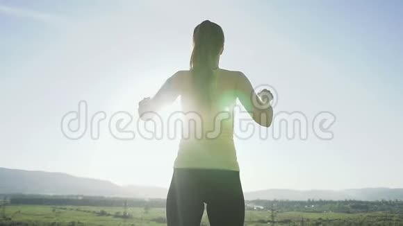 年轻的运动女性站在悬崖边缘举起双手在日落时跳上山顶快乐视频的预览图