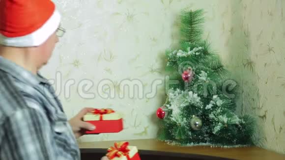 一个戴圣诞老人帽子的人正在圣诞树下放圣诞礼物视频的预览图