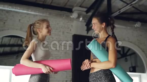 漂亮的女孩在大型现代体育中心谈笑风生女人们拿着五颜六色的瑜伽垫视频的预览图