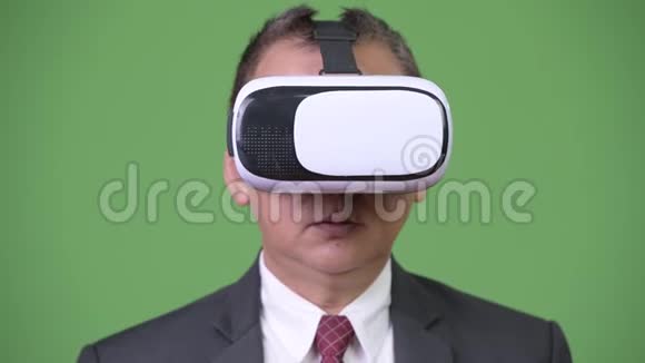 成熟的日本商人在绿色背景下使用虚拟现实耳机视频的预览图
