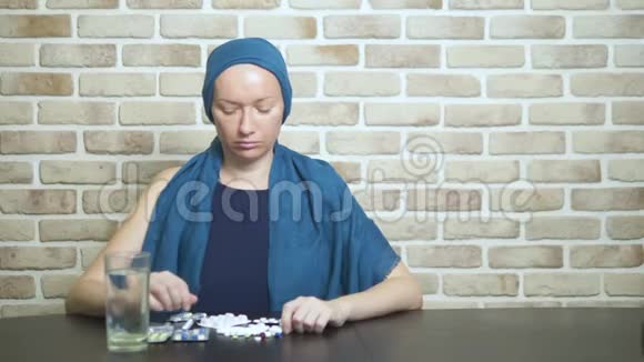 一个戴头巾的女人一个癌症病人碰了碰药片坐在靠着砖墙的桌子旁复制空间视频的预览图
