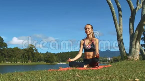女孩用瑜伽姿势对抗绿色海岸蓝天视频的预览图