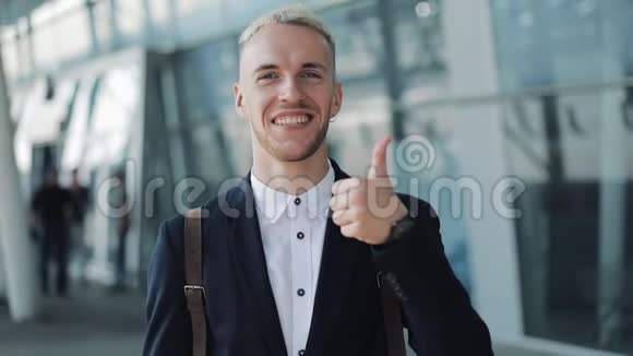 由年轻有魅力的商人在办公室外竖起大拇指快乐的人站在机场附近看镜头视频的预览图