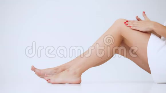 年轻女子双腿特写女孩按摩她酸痛的膝盖摩擦奶油孤立地坐在白色的背景上视频的预览图