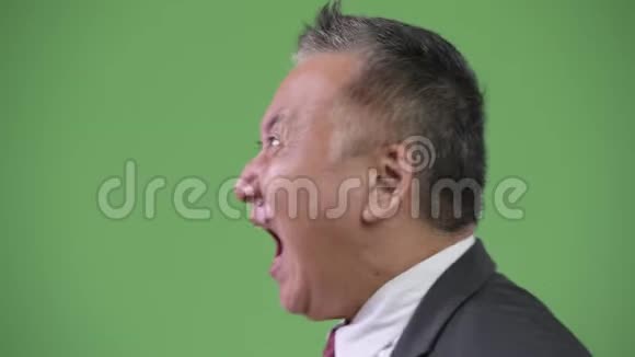 成熟愤怒的日本商人在绿色背景下呐喊的侧写视频的预览图