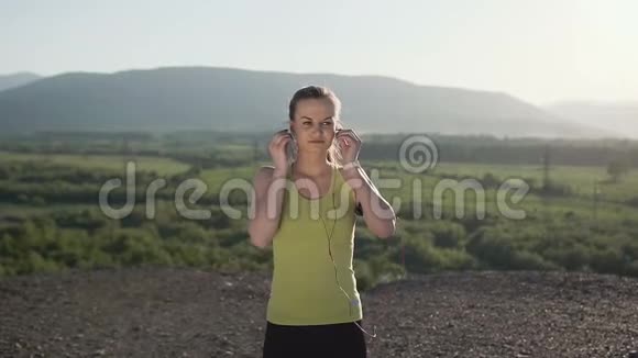 骑着相机一个在日落时分在山上慢跑的女运动员她戴着耳机听音乐视频的预览图