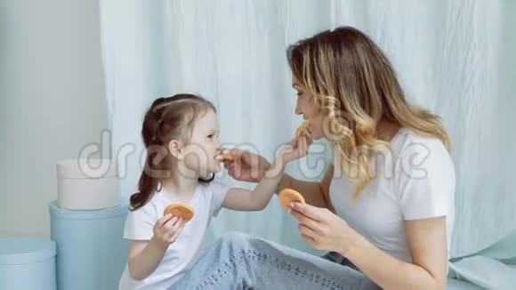 妈妈和小女孩互相喂饼干一个有个小女儿的女人坐在地板上年轻的母亲视频的预览图