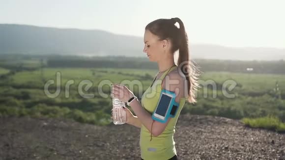 健身年轻女性从运动瓶中饮水在山上户外跑步训练后的冷饮合身女孩视频的预览图