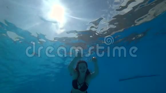 睁开眼睛的女人在充满活力的环境中缓慢地漂浮在水下进入蓝色的游泳池视频的预览图