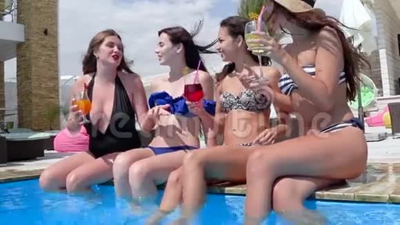 参加夏季派对的朋友们喝着五颜六色的饮料的女孩在蓝色游泳池的露台上水中溅起双腿视频的预览图