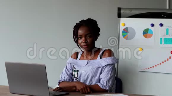 一个美国黑人漂亮女孩坐在笔记本电脑上穿着办公室服装在图形背景上的肖像视频的预览图