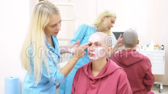 在美容师的约会中时髦的秃头女人在脸上涂上麻醉霜视频的预览图
