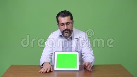 英俊的波斯胡子男医生一边说一边展示数字平板电脑视频的预览图