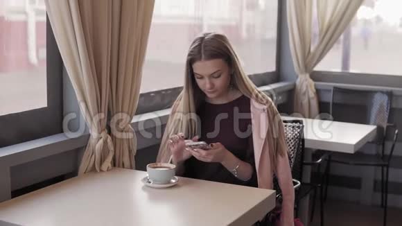 美丽的女孩短信和喝咖啡在城市咖啡馆喝咖啡的女人视频的预览图