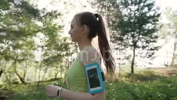 高加索裔年轻女性在森林里的户外用智能手机在耳机上跑步和听音乐视频的预览图