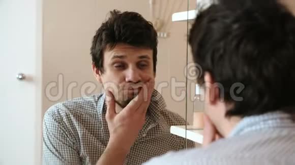 刚刚醒来的疲惫的男人刷牙看着镜子里的倒影看到他邋遢的样子视频的预览图