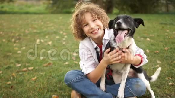 男孩拥抱和抚摸他自制的黑白狗坐在公园的草地上一幅近距离的肖像画视频的预览图