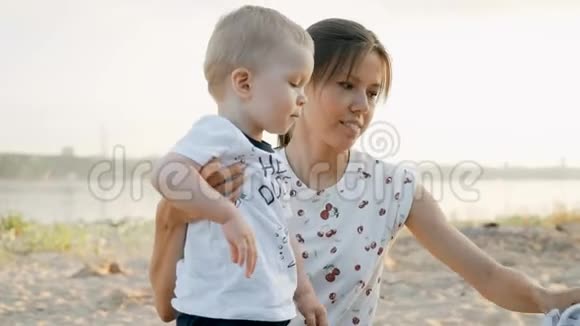 日落时分年轻的母亲和她的小儿子在海滩上慢动作视频的预览图