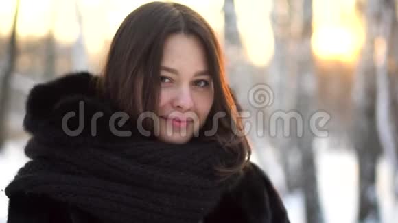 在冬季霜林户外身穿黑色毛皮大衣和针织大围巾的美丽黑发女孩的特写肖像视频的预览图