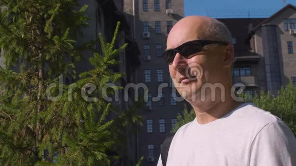 城市中戴太阳镜的成年男子在智能手机上发短信聊天视频的预览图