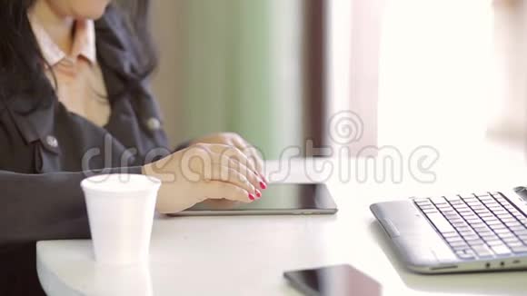 女性的手在平板电脑上做特写旁边是一台笔记本电脑和一杯一次性咖啡视频的预览图