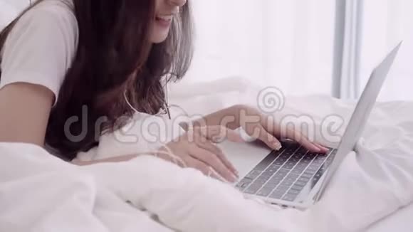 美丽迷人的亚洲女人的肖像使用电脑或笔记本电脑和听音乐躺在床上放松时视频的预览图