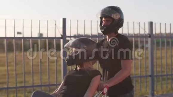 日落时分一个穿着摩托车头盔的男人在手推车里翻滚着迷人的年轻女人慢动作有趣的一对视频的预览图