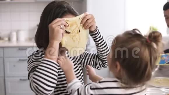 有趣的母亲正在和她的小女儿玩她的脸上戴着煎饼做滑稽的面具家庭早餐视频的预览图
