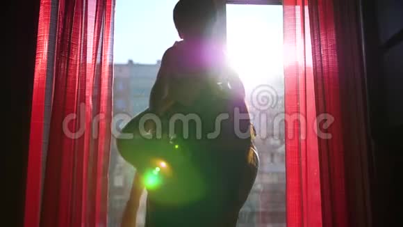 一位年轻而快乐的母亲正把她的孩子抱在窗户旁边太阳光线穿过窗户笑声视频的预览图