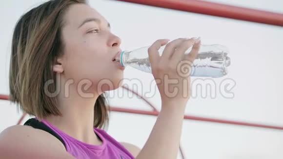 年轻健康的运动员坐在体育场讲台上的瓶子里喝水视频的预览图