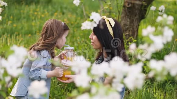 妈妈和一个小女儿在春天的花园里喝橙汁视频的预览图