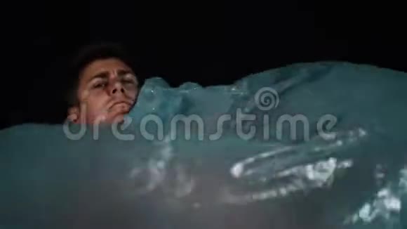 躺在蓝色玻璃纸下的年轻人模仿水潜水和喷水视频的预览图