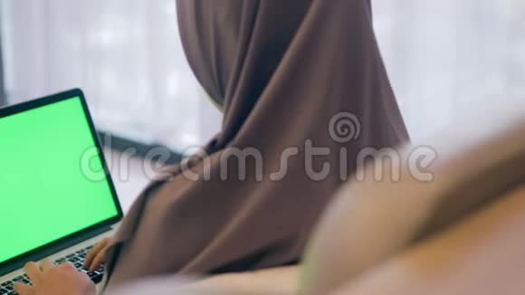 穆斯林妇女坐在绿色屏幕笔记本电脑上工作的后视图视频的预览图