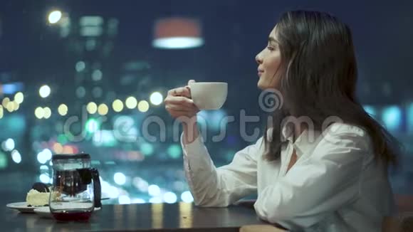 女孩喝茶欣赏深夜坐在舒适的咖啡馆里的夜城景色视频的预览图